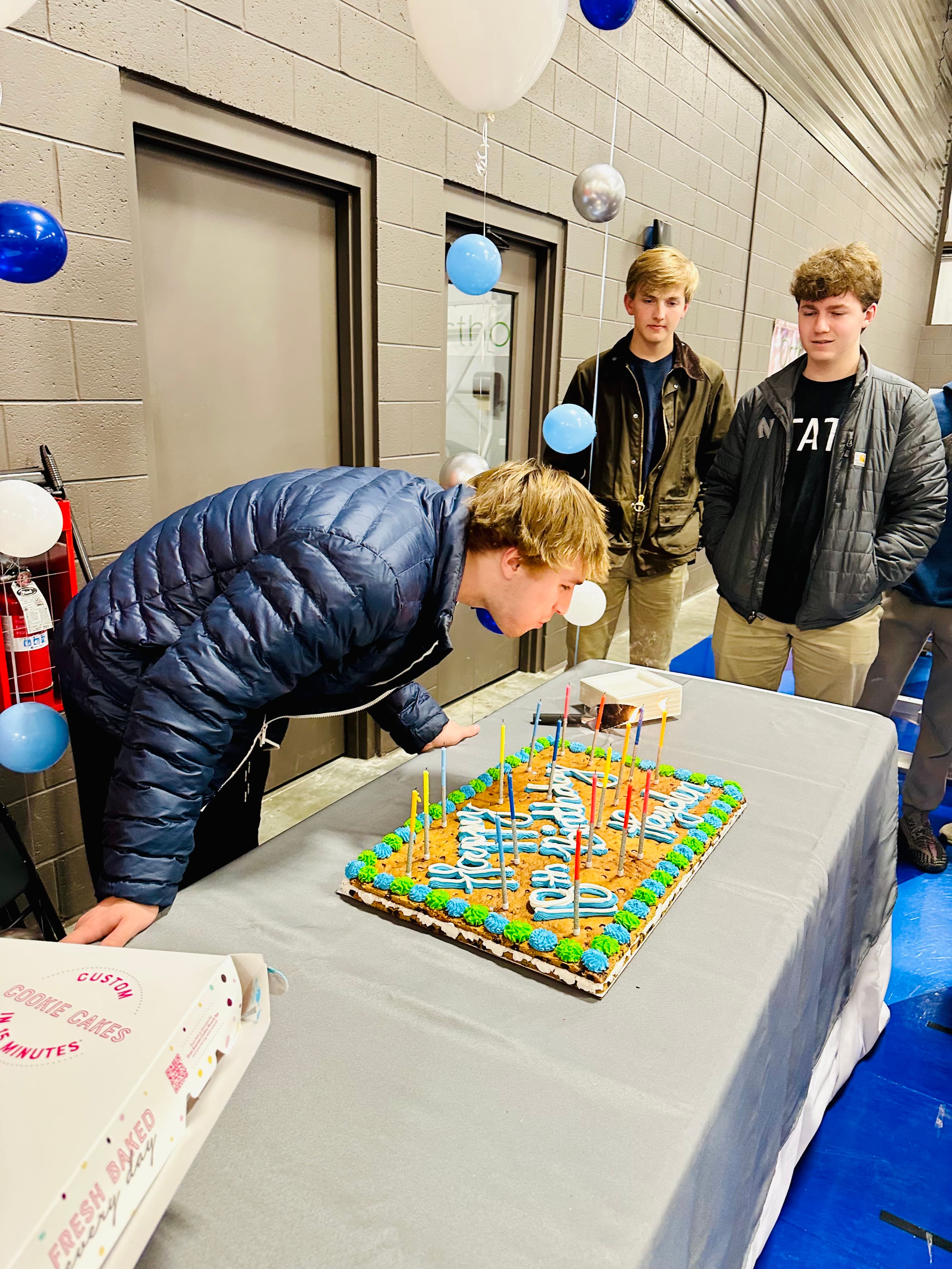 Birthday boy blowing out candles on a basketball-themed cake at The Net District