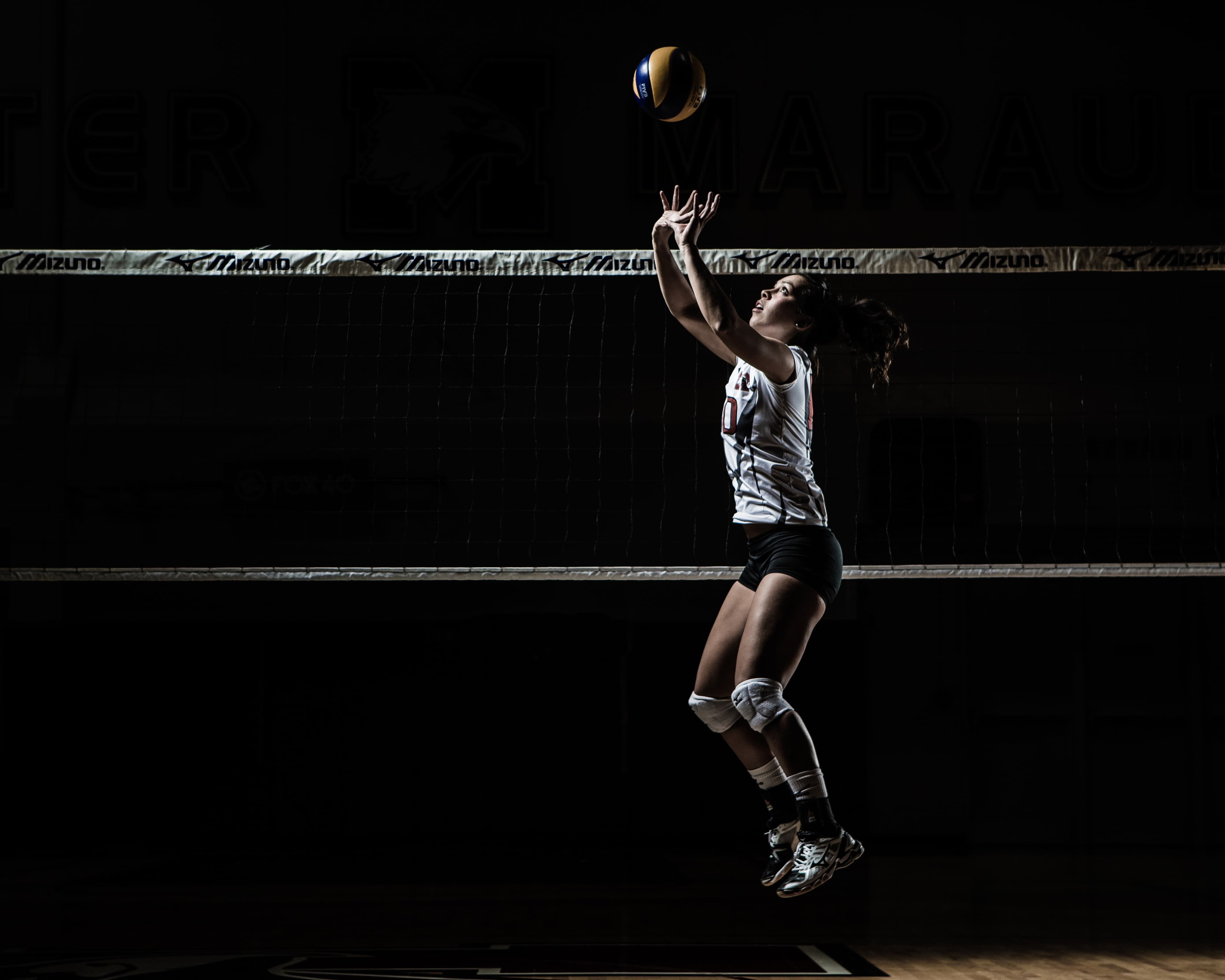 Volleyball player setting at the net under a single hard light